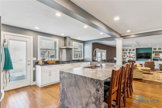 3114 Gleneagle Dr, Findlay, OH 45840 - kitchen with decorative columns, wall chimney range hood, dark stone counters, light wood-style flooring, and stainless steel gas stovetop