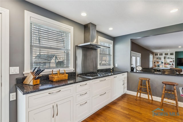 3114 Gleneagle Dr, Findlay, OH 45840 - kitchen with stainless steel gas cooktop, wood finished floors, dark stone counters, wall chimney exhaust hood, and white cabinets
