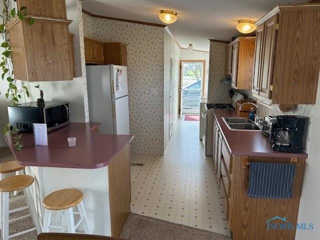 kitchen featuring wallpapered walls, stainless steel microwave, light floors, a sink, and freestanding refrigerator