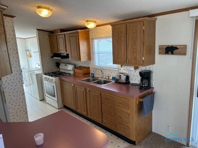 kitchen featuring gas range gas stove, under cabinet range hood, a sink, washer and dryer, and light floors