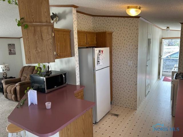 kitchen with a textured ceiling, ornamental molding, stainless steel microwave, and freestanding refrigerator