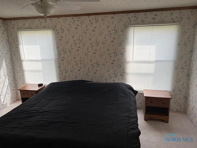 bedroom featuring crown molding, carpet floors, a textured ceiling, wallpapered walls, and ceiling fan