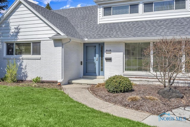 entrance to property with a lawn, a shingled roof, and brick siding