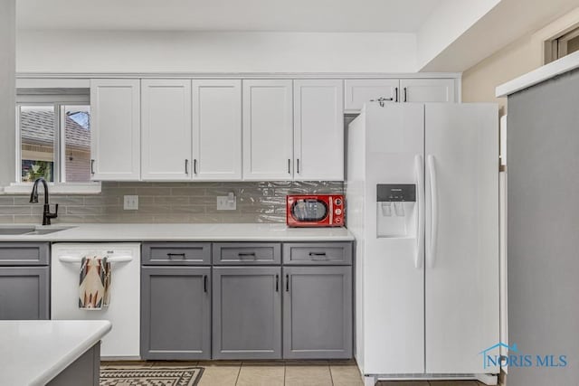 kitchen featuring gray cabinets, light countertops, a sink, tasteful backsplash, and white appliances