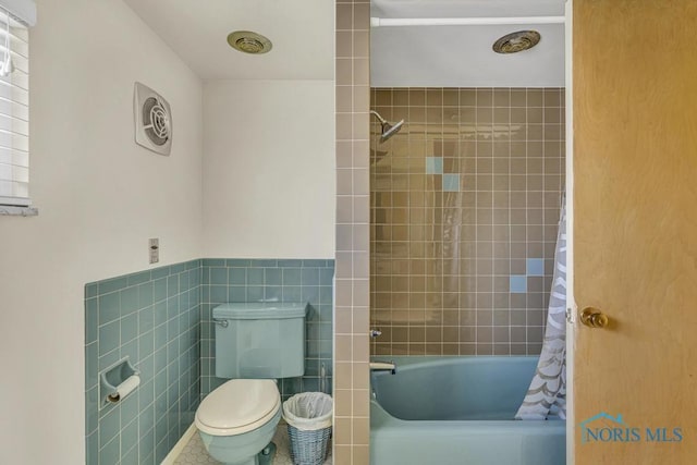 full bathroom featuring a wainscoted wall, toilet, shower / tub combo with curtain, and tile walls