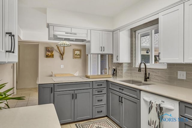 kitchen featuring light countertops, under cabinet range hood, a sink, white dishwasher, and gray cabinets