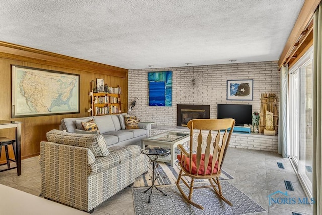 living room featuring a textured ceiling, wood walls, brick wall, and a brick fireplace