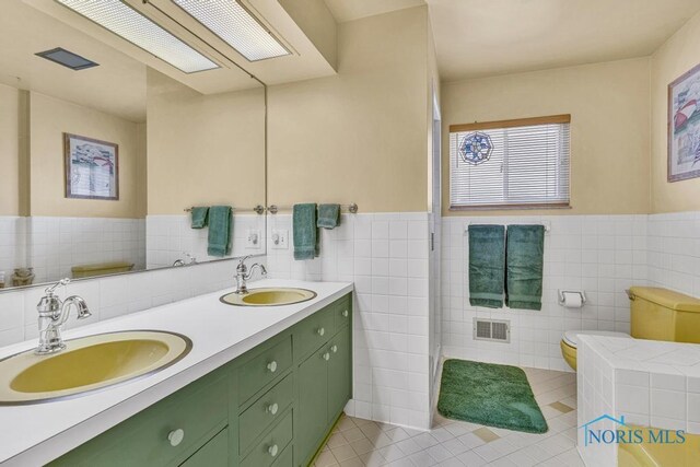bathroom with tile walls, visible vents, and a sink