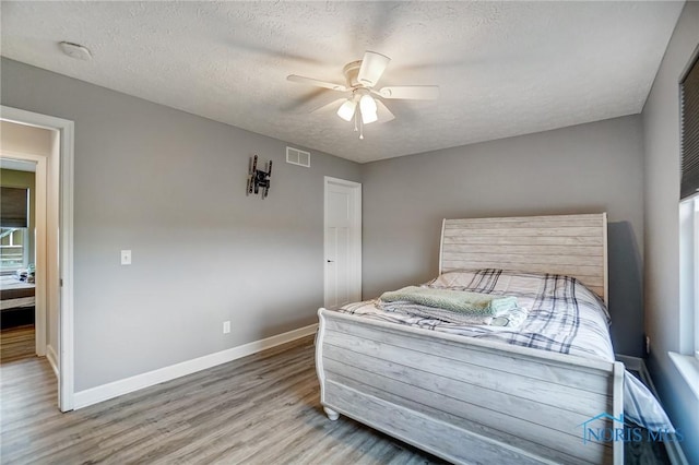 bedroom with baseboards, visible vents, wood finished floors, and a textured ceiling
