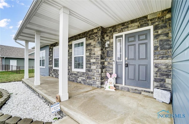 doorway to property with fence, covered porch, and stone siding