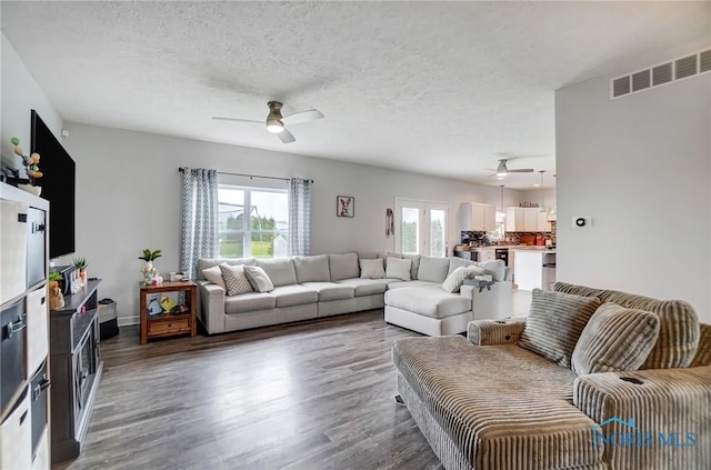 living room featuring wood finished floors, visible vents, a textured ceiling, and ceiling fan