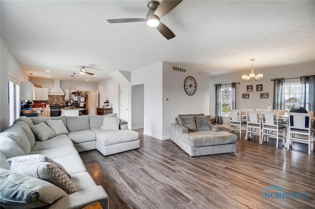 living area featuring dark wood-style flooring, ceiling fan with notable chandelier, baseboards, a textured ceiling, and visible vents