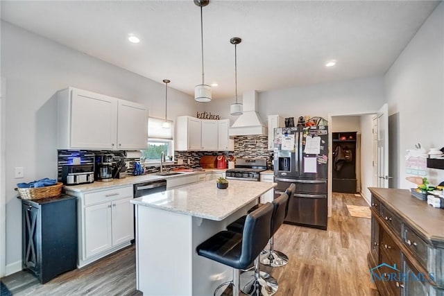 kitchen with stainless steel appliances, custom range hood, white cabinets, light wood-style floors, and decorative backsplash