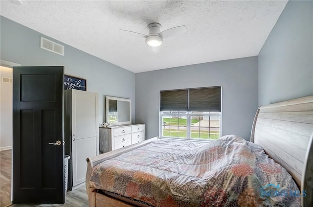 bedroom with a textured ceiling, visible vents, ceiling fan, and wood finished floors