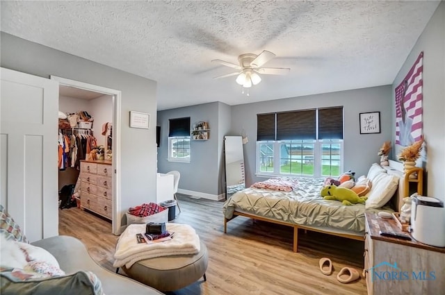 bedroom featuring a ceiling fan, a walk in closet, a textured ceiling, and wood finished floors