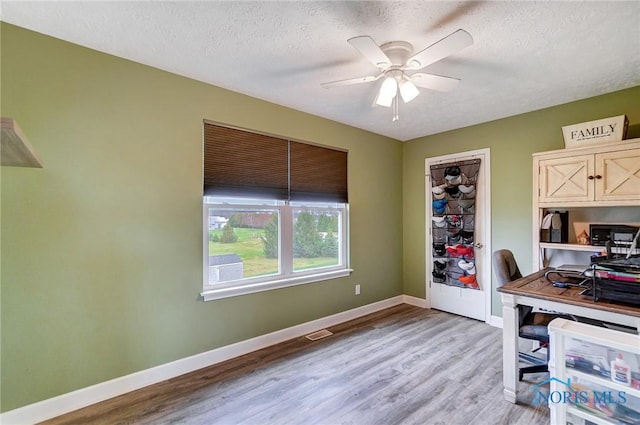home office with light wood finished floors, a textured ceiling, baseboards, and a ceiling fan
