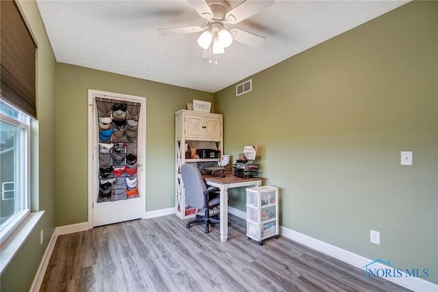 unfurnished office featuring a textured ceiling, visible vents, baseboards, ceiling fan, and light wood-style floors