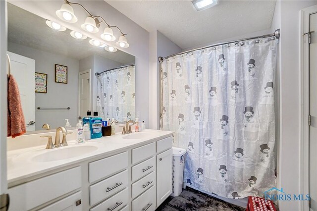 full bathroom with a shower with curtain, double vanity, a sink, and a textured ceiling