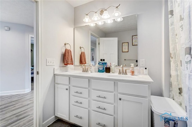 full bathroom with double vanity, a sink, baseboards, and wood finished floors