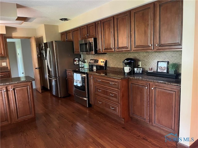 kitchen with dark wood-style floors, stainless steel appliances, dark stone counters, and tasteful backsplash