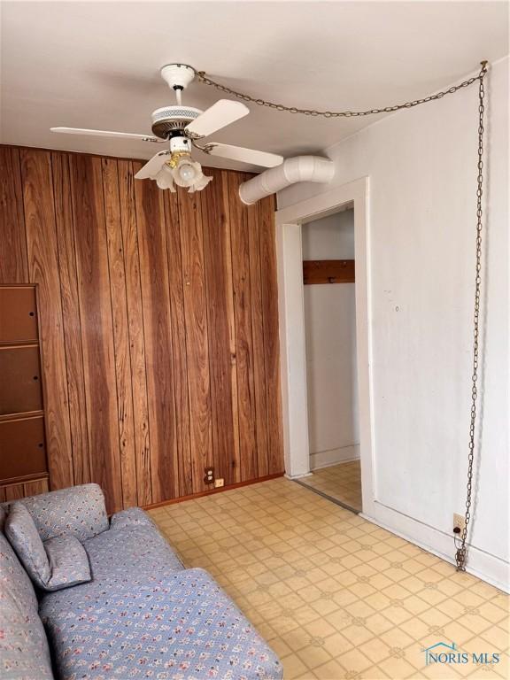 bedroom with ceiling fan, wood walls, and light floors