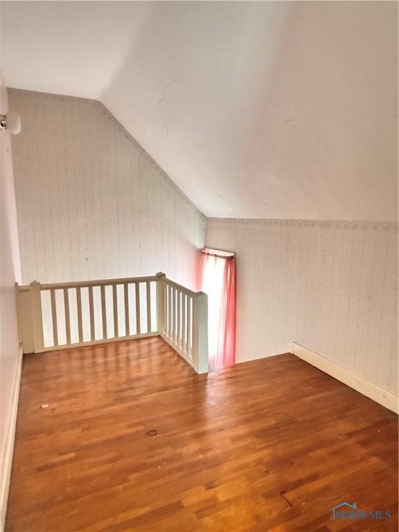 bonus room featuring baseboards, wallpapered walls, wood finished floors, and vaulted ceiling