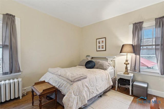 bedroom with radiator heating unit, wood finished floors, and baseboards