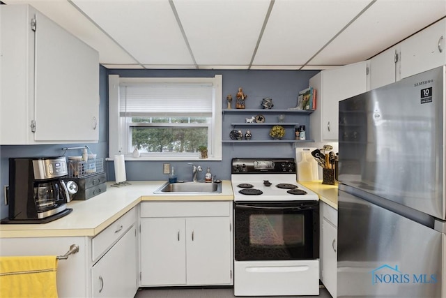 kitchen featuring light countertops, freestanding refrigerator, white cabinets, electric stove, and a sink