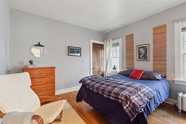 bedroom featuring wood finished floors, radiator heating unit, baseboards, and multiple windows