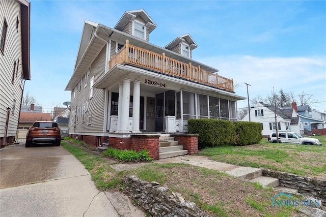 view of front of house featuring driveway, a balcony, and a sunroom