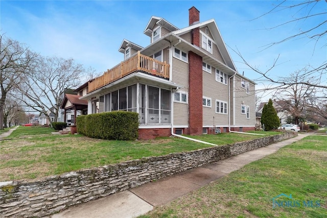 view of side of property featuring a yard, a sunroom, a balcony, and a chimney