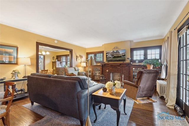living room with a chandelier, radiator heating unit, dark wood-style flooring, and a brick fireplace