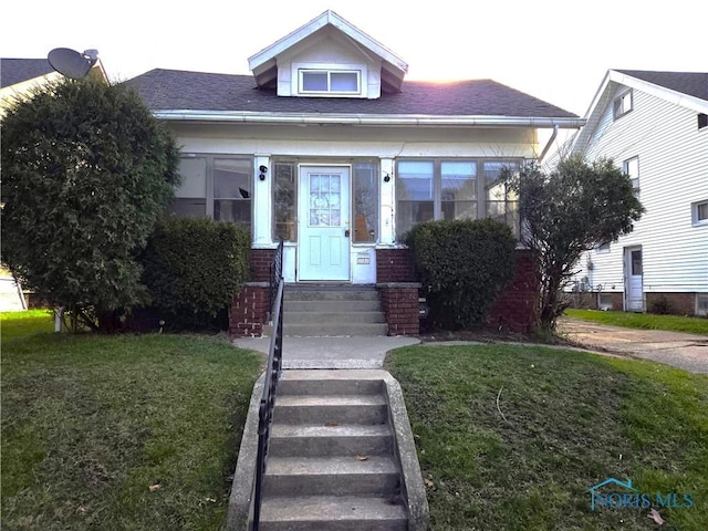 bungalow with a front yard and roof with shingles