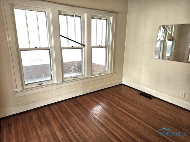 spare room featuring dark wood-style flooring, visible vents, and baseboards