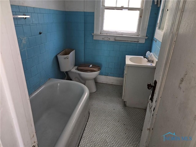 full bath with a bath, vanity, tile patterned flooring, toilet, and tile walls