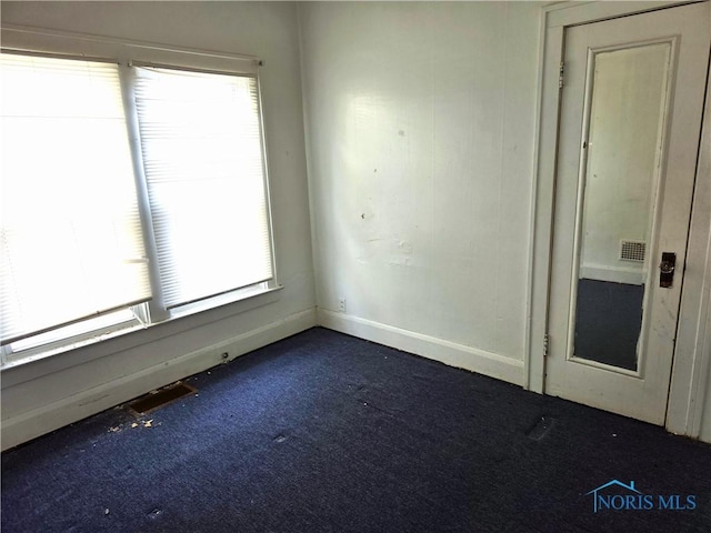 spare room featuring visible vents, dark colored carpet, and baseboards