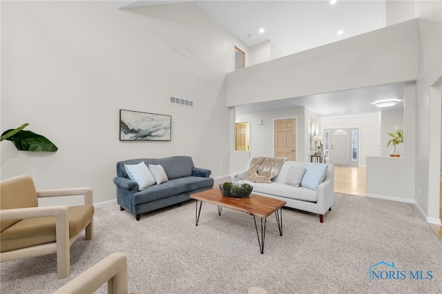 living area with a high ceiling, baseboards, visible vents, and light colored carpet