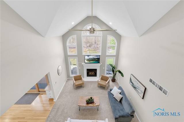 living room with high vaulted ceiling, baseboards, visible vents, a ceiling fan, and a glass covered fireplace
