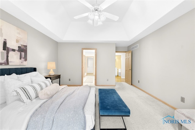 carpeted bedroom featuring baseboards, a tray ceiling, visible vents, and connected bathroom