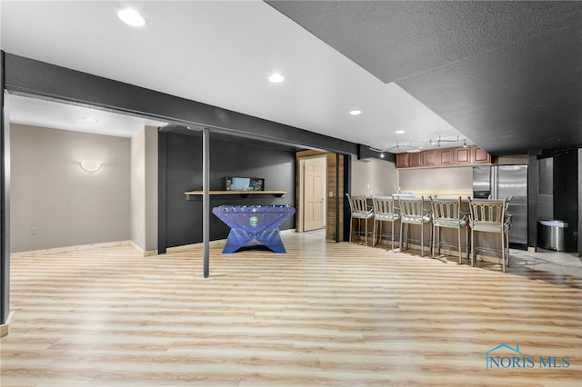bar with light wood-style flooring, baseboards, indoor bar, recessed lighting, and stainless steel fridge with ice dispenser