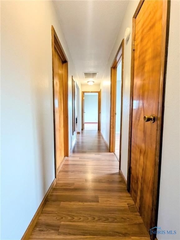 hall featuring visible vents, baseboards, and wood finished floors