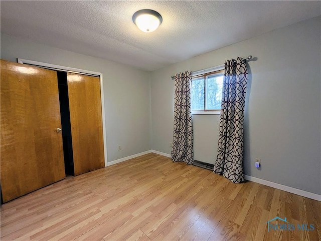 unfurnished bedroom with baseboards, a textured ceiling, a closet, and wood finished floors