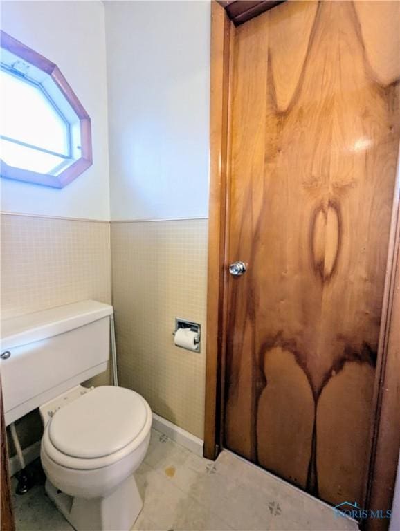 bathroom with tile walls, a wainscoted wall, and toilet