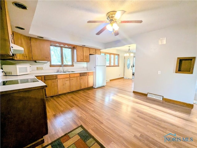 kitchen with white appliances, ceiling fan with notable chandelier, under cabinet range hood, a sink, and visible vents