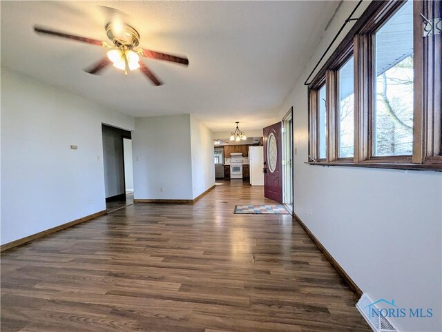 unfurnished living room with baseboards, ceiling fan with notable chandelier, and dark wood-style flooring