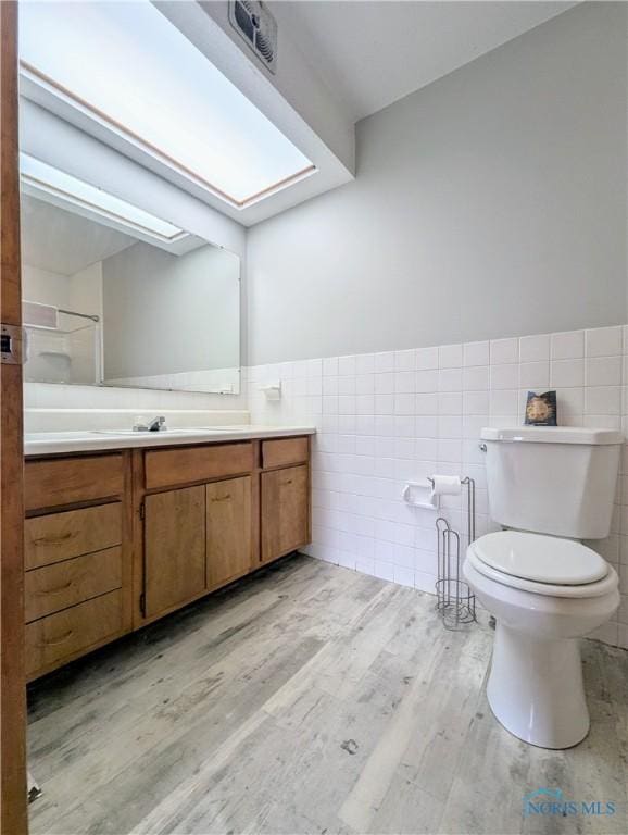 bathroom with toilet, vanity, wood finished floors, wainscoting, and tile walls