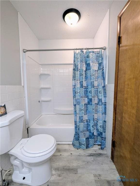 full bath featuring a wainscoted wall, toilet, wood finished floors, shower / tub combo, and tile walls