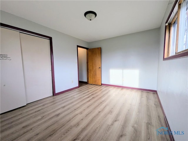 unfurnished bedroom with baseboards, light wood-type flooring, and a closet