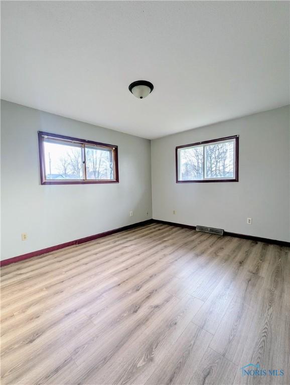empty room featuring baseboards, light wood finished floors, and visible vents