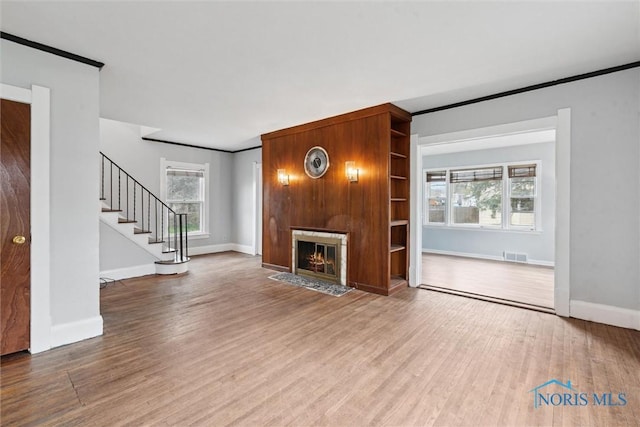 unfurnished living room featuring baseboards, wood finished floors, visible vents, and ornamental molding
